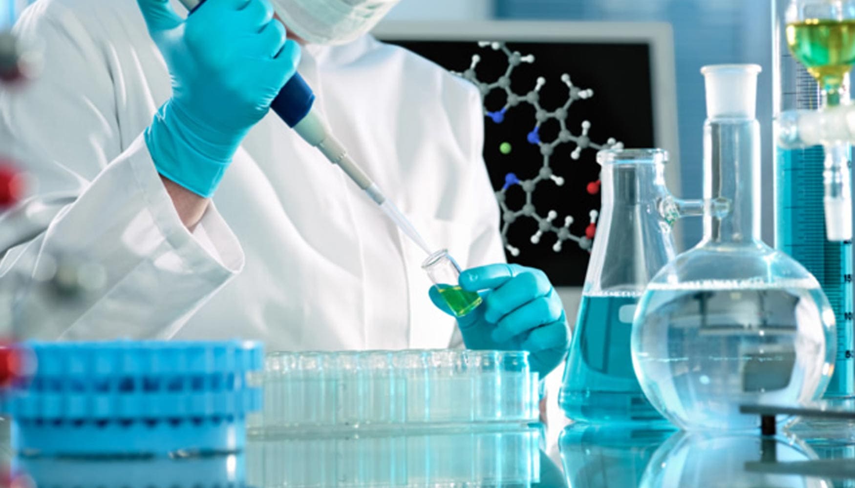 Persona con bata de laboratorio y guantes sostiene un tubo de ensayo.