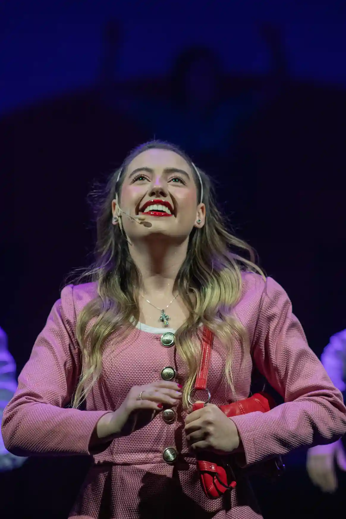 Mujer sonriente con traje rosa sosteniendo un bolso rojo.