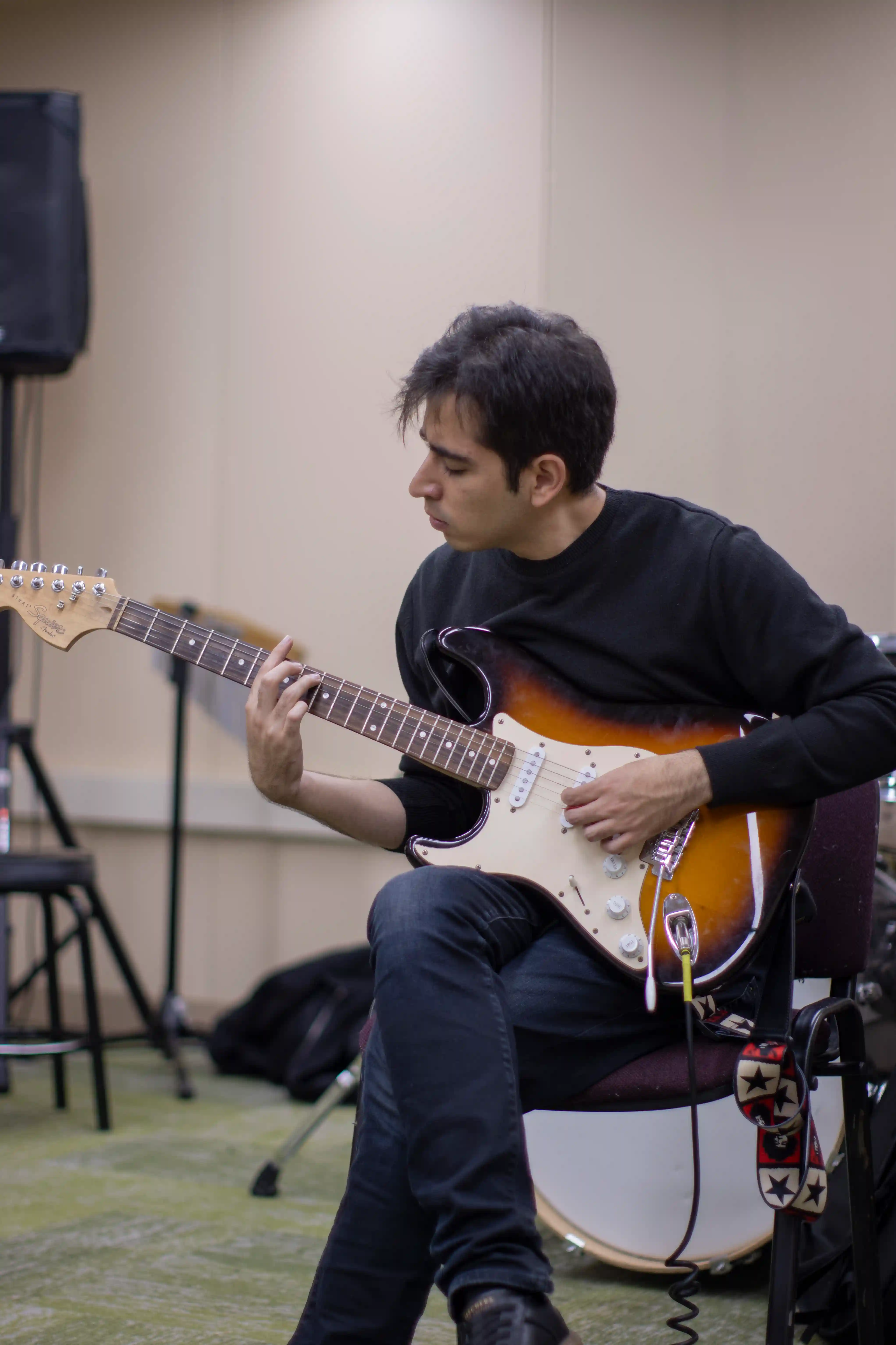 Un hombre sentado, tocando la guitarra con pasión, rodeado de un ambiente musical.