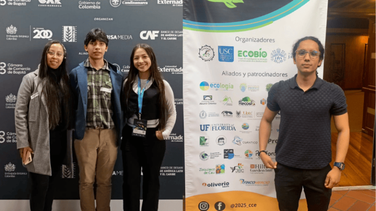 Tres personas de pie juntas frente a un banner de logos.