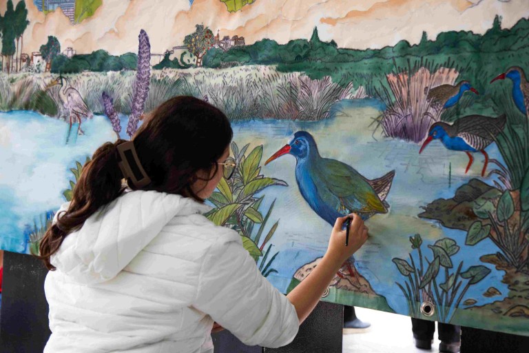 Estudiante de Artes Plásticas de la Universidad El Bosque detalla aves acuáticas nativas del Río Bogotá en el mural sobre biodiversidad y recuperación ambiental.
