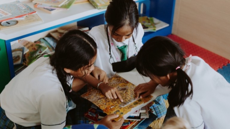 Niñas en uniforme escolar leyendo un libro juntas en el colegio