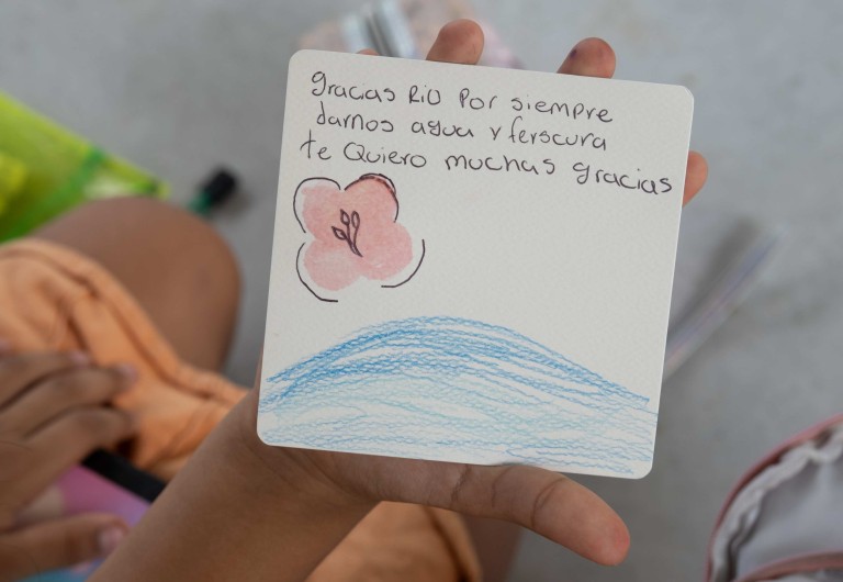 Niño de Guachaca sostiene una carta dibujada a mano con el mensaje 'Gracias río por siempre darnos agua y frescura', resultado de los talleres del proyecto Ríos Viajeros de la Universidad El Bosque