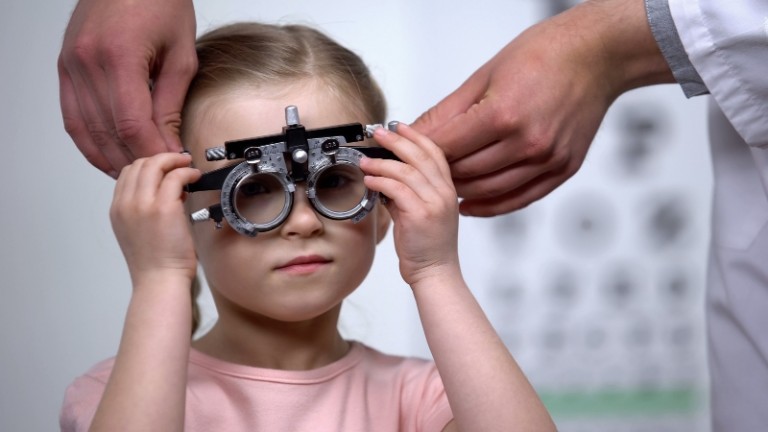Niña mira a través de una montura de prueba durante un examen de optometría