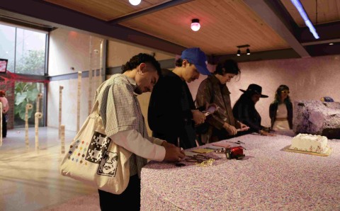 Estudiantes observan y participan en una instalacion artistica con mesa cubierta de confeti y una torta en la exposicion de Artes Plasticas de la Universidad El Bosque.