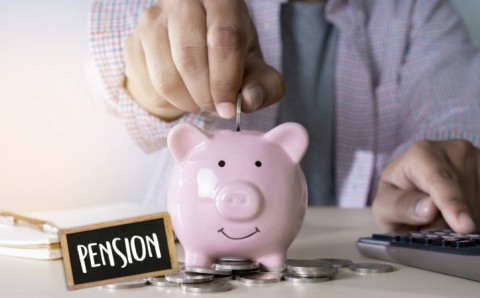 Persona depositando moneda en alcancía rosada junto a letrero de pensión y calculadora, simbolizando el ahorro pensional en Colombia
