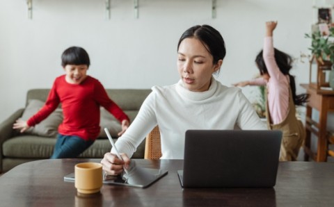 Madre trabajando en su computador portátil mientras dos niños juegan sin supervisión