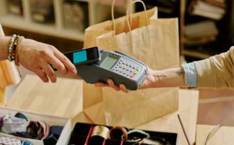 Persona pagando con celular en un datáfono, ilustrando el pago electrónico de la declaración de renta