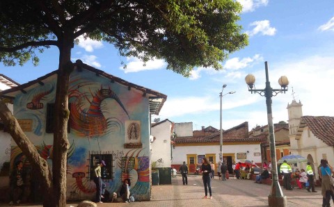 Plaza en el barrio La Candelaria de Bogotá, con una casa pintada con mural y personas caminando