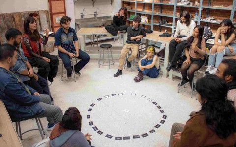 Estudiantes de Artes Plásticas sentados en círculo alrededor de tarjetas dispuestas en el piso.