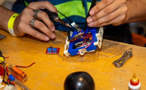 Manos de un competidor sueldan los circuitos de un robot sobre una mesa de trabajo durante el torneo de robótica.